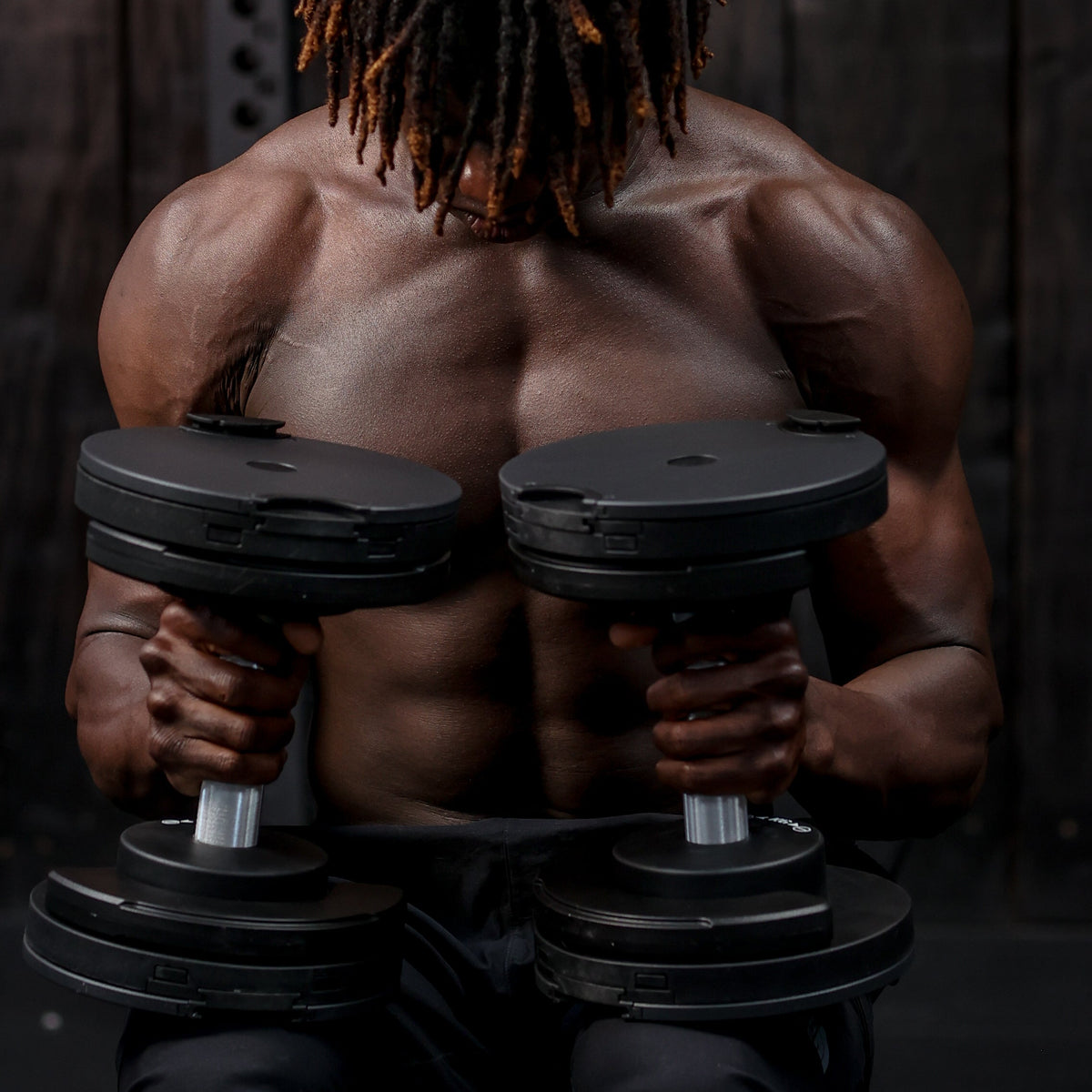 Muscular person holding dumbbells in a dark setting