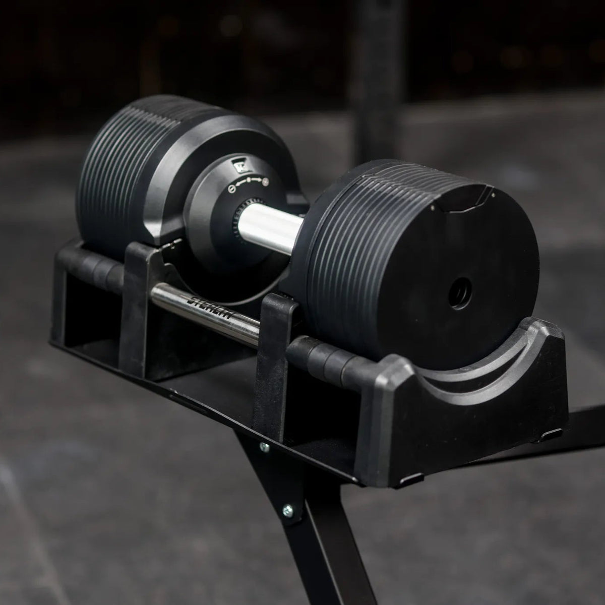 Stealth Adjustable Dumbbells Black Edition resting in its cradle on the stand in a dark gym - Assassin Goods